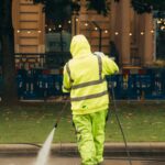 A city worker in high-visibility gear pressure washing a street corner. victoria bc