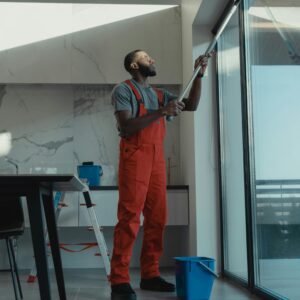 A man in coveralls cleans a large window in a stylish, modern home interior in victoria, canada